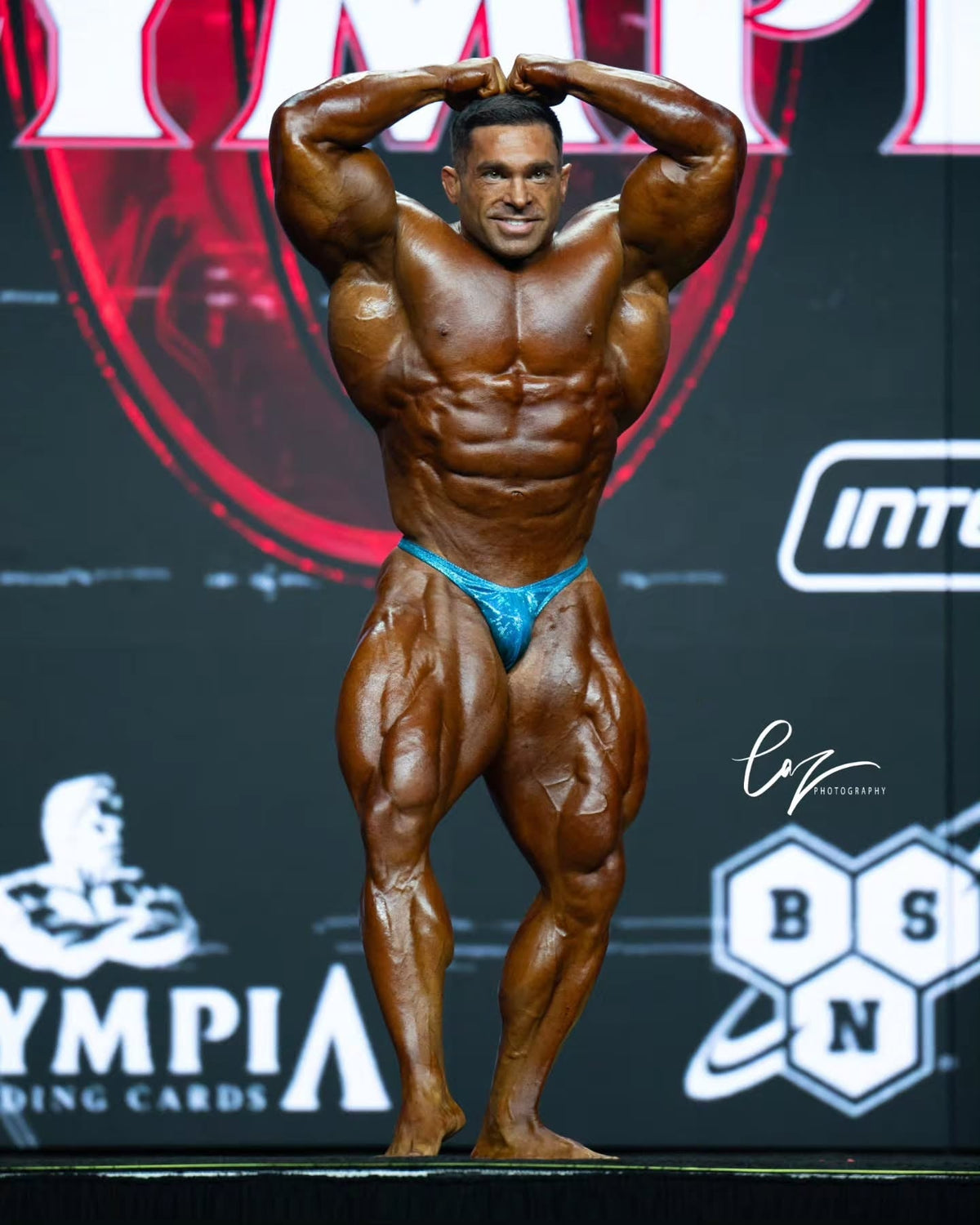 Derek Lunsford on the 2026 Olympia stage in turquoise bodybuilding trunks by SY Competition Suits