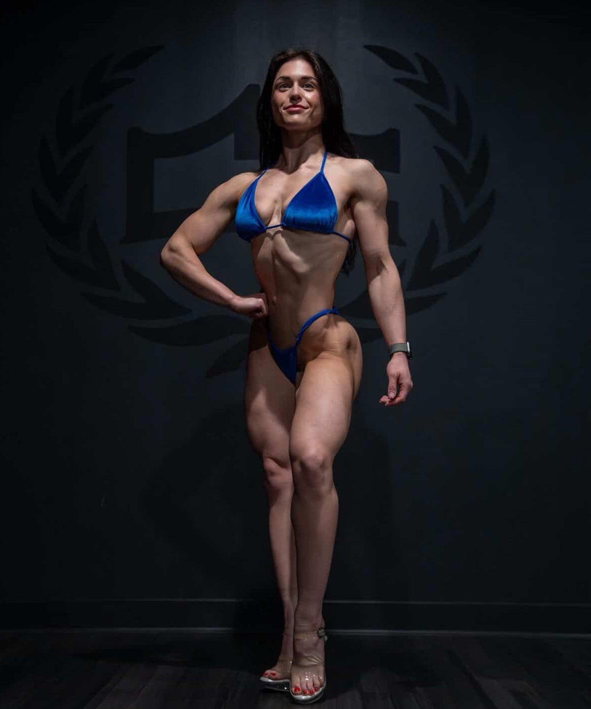 Front view of NPC competitor practicing in a royal blue velvet posing suit with adjustable slide sides
