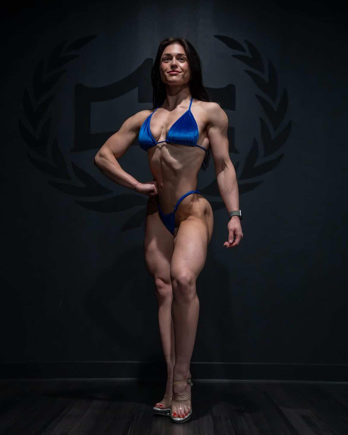 Front view of NPC competitor practicing in a royal blue velvet posing suit with adjustable slide sides
